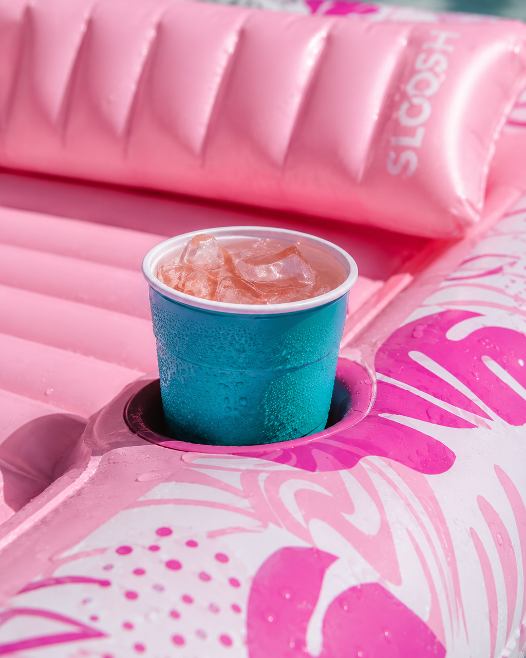 Blue cup with a drink on a pink inflatable tanning pool with flamingo design