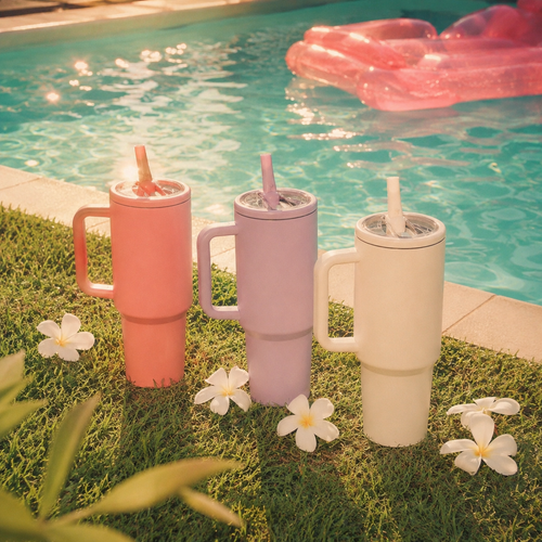 Three colorful tumblers with straws on grass by a pool