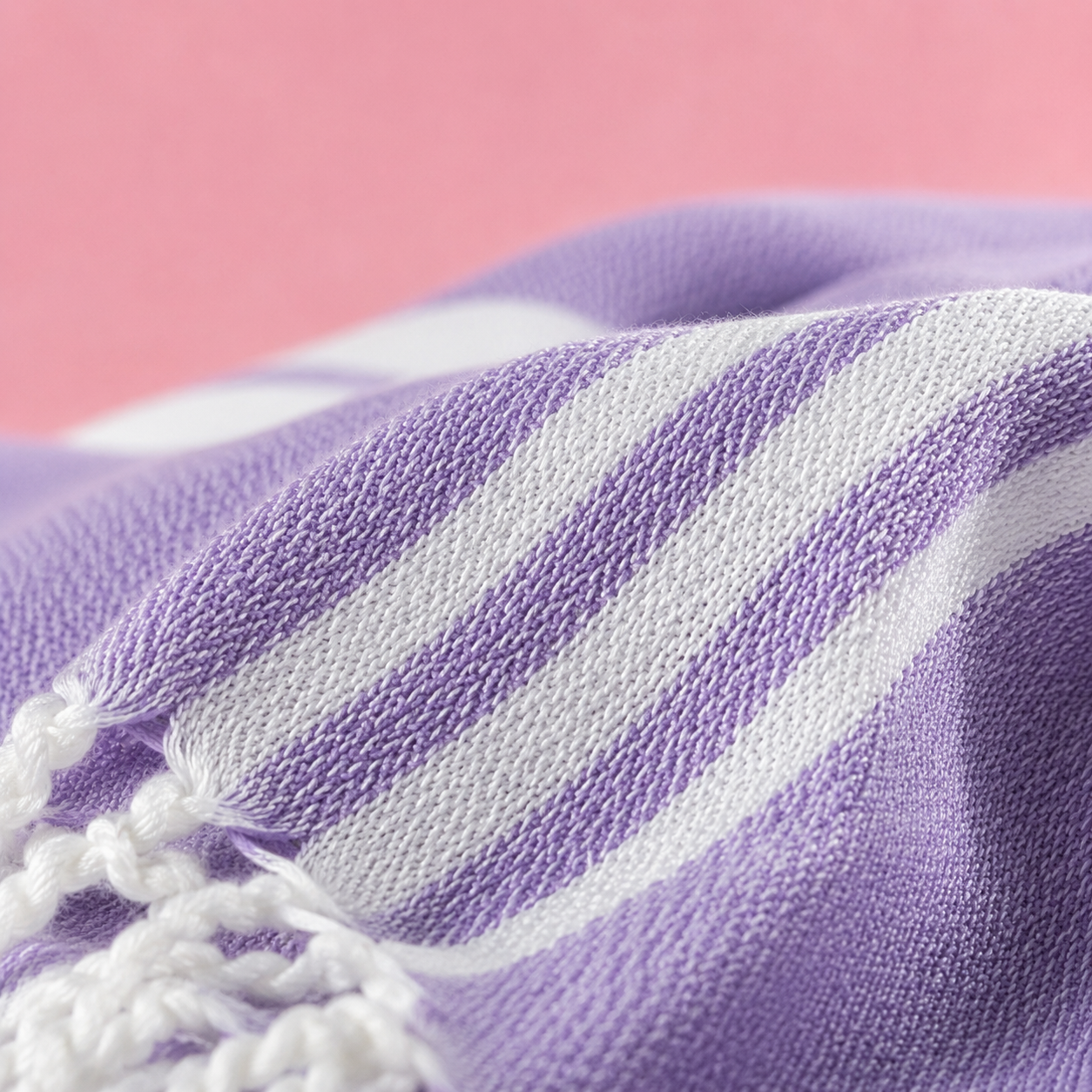 Close-up of a purple and white striped towel with tassels on a pink background